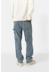 Hellblaue Denim-Cargo-Hosen mit mehreren Taschen, geradem Bein und einem ausgewaschenen Effekt. Kombiniert mit einem weißen Langarmshirt und beigen Sneakern.