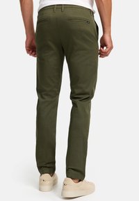 Pantalones verde oliva hechos de tejido suave, con dos bolsillos traseros y un diseño ajustado. Combinados con zapatillas de color claro.