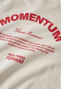 Röd text på beige tyg med orden "MOMENTUM," "Vibrant Movement," och motiverande fraser om framsteg och att driva saker framåt.