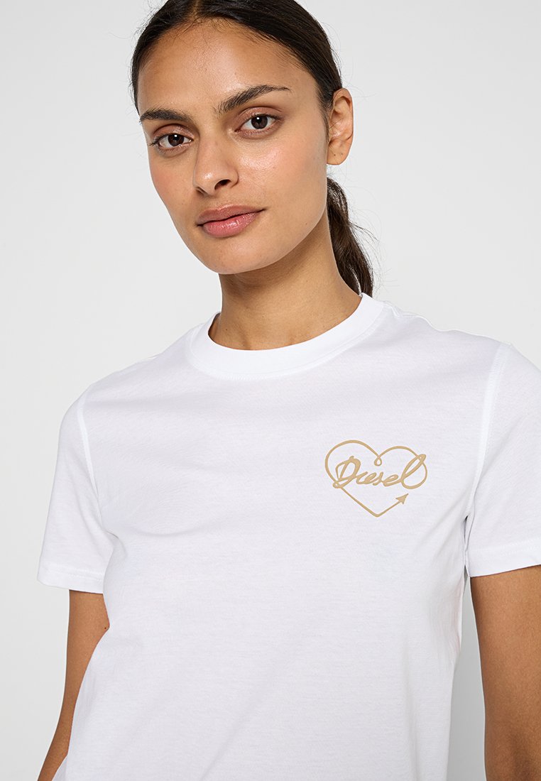 Biała bawełniana koszulka z grafiką złotego serca z napisem "Diesel" i detalem w postaci strzałki. Okrągły dekolt i krótkie rękawy. Gładka tekstura.