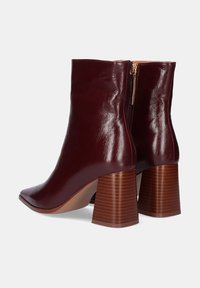 Botas de tobillo burdeos de cuero brillante, con punta afilada y tacón de bloque de madera acanalado, con una cremallera lateral para el cierre.