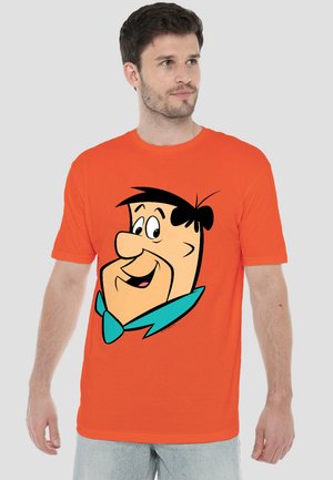 Man wearing orange t-shirt with large cartoon face of Fred Flintstone smiling, on a plain light gray background.