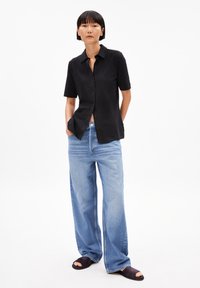Black short-sleeve button-up shirt, paired with light blue wide-leg jeans, and dark sandals. Smooth fabric with a classic collar design.