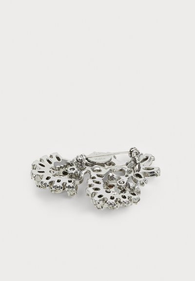 Silver-toned brooch featuring two intertwined leaf designs with cut-out patterns and textured edges, secured with a pin clasp.