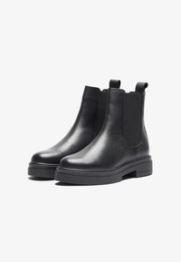 Botas de cuero negro hasta el tobillo con paneles laterales elásticos, punta redondeada y superficie texturizada. Suela de goma gruesa con un sutil pespunte de contraste.