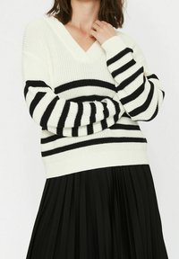 Svart- och vitrandig stickad tröja med v-hals, med en strukturerad design och ribbade ärmslut, kombinerad med en svart plisserad kjol.