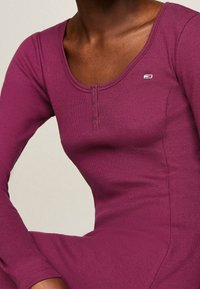 Langärmliges Kleid aus geripptem Stoff in tiefpurpurfarbe, mit Rundhalsausschnitt und Knopfdetails auf der Vorderseite. Kleines Logo-Detail auf der Brust.