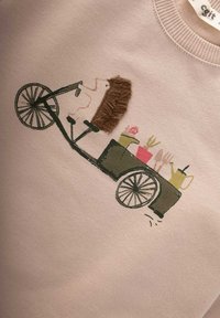 Svetlo roza sweatshirt s ilustracijo ježa na kolesu, ki ima v vozičku vrtnarske pripomočke. Mehka tkanina, sproščen dizajn.