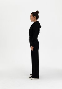 Mustan hupparin, jossa on joustava vyötärö ja yhdistelevät verkkarit. Sileä kangas, rento istuvuus, sivutaskut ja kontrastiväriset platform-kengät.