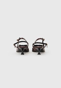 Glossy burgundy patent leather heels with two slim ankle straps and a black flared heel. Features a contrasting gold-tone buckle detail.