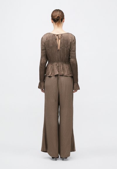 Barna peplum felső texturált anyagból, hosszú ujjakkal és kulcslyukas hátrésszel. Széles szárú, hozzá illő barna nadrággal párosítva.