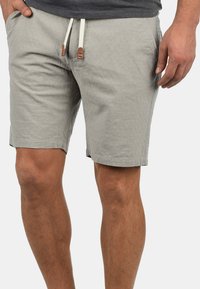 Shorts gris clair en tissu texturé. Comprend un cordon de serrage avec des accents en bois, des poches latérales et une coupe décontractée.