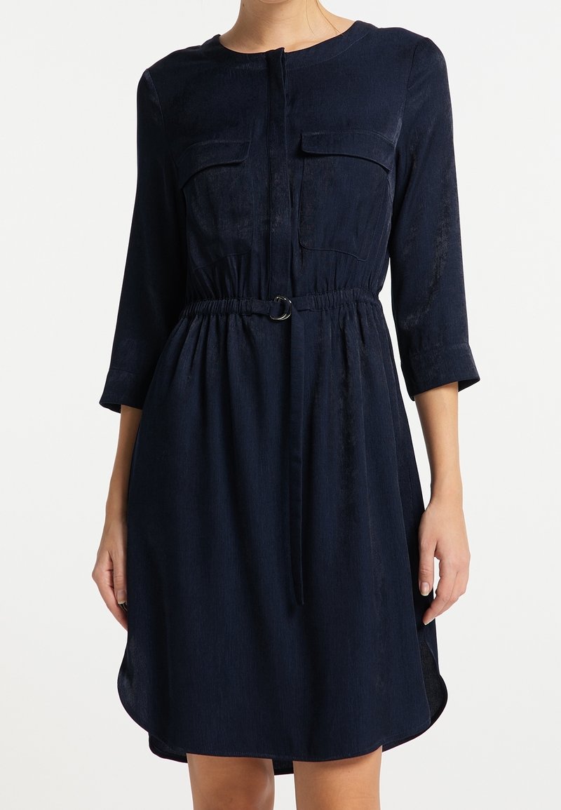 Vestido azul marino con escote redondo, cierre de botones, dos bolsillos en el pecho, cintura ajustada con un cinturón y mangas de tres cuartos. Textura suave.
