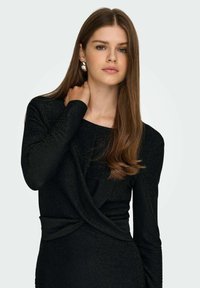 Czarny top z długim rękawem wykonany z tkaniny o fakturze, z przodem zawiązanym w skręt. Gładkie wykończenie z subtelnym połyskiem. Okrągły dekolt.