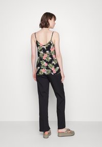 Top preto sem mangas com um padrão floral apresentando folhas rosas e verdes, combinado com calças pretas de perna reta e sandálias verdes.