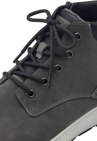 Bottine en cuir gris, avec un bout rond, des lacets noirs, des œillets en métal et des coutures décoratives. Semelle en caoutchouc avec un motif de traction.