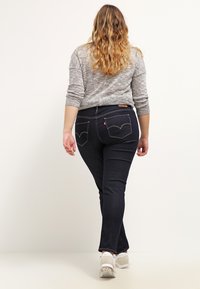 Tamno plave traperice od denima, s uskim krojem, stražnjim džepovima s detaljima šivanja, nosene s sivim puloverom i bijelim tenisicama.