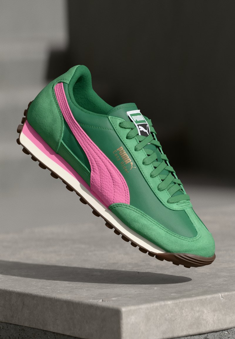 Sneaker atletica verde e rosa realizzata in materiali scamosciati e sintetici, con punta rotonda e striscia laterale rosa testurizzata. Presenta una suola intermedia bianca e una suola esterna marrone.