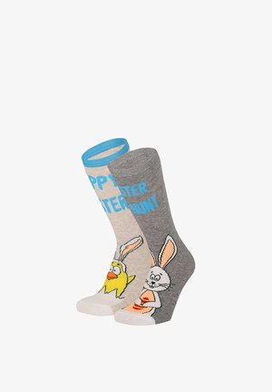 Two Easter-themed socks, one grey with a bunny holding an egg, one beige with a chick wearing bunny ears and blue text.