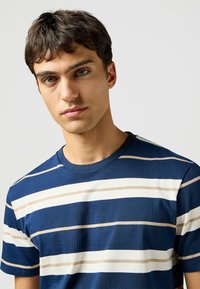 Camiseta de cuello redondo a rayas en azul marino con rayas horizontales alternas en beige y blanco. Material de algodón, manga corta, textura suave.