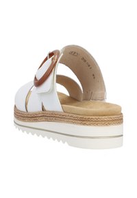 White leather sandal featuring a wide strap, circular brown accent, and a textured sole with a tapered edge for stability.