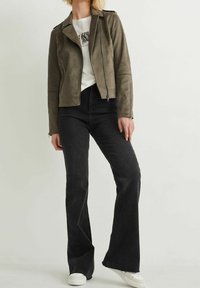 Veste de moto en daim vert olive avec des détails zippés, associée à un jean noir évasé taille haute et des baskets blanches.