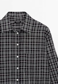 Czarna i biała koszula w kratę z guzikami, z zaostrzonym kołnierzykiem, kieszenią na piersi oraz białymi guzikami; lekki materiał o gładkiej teksturze.