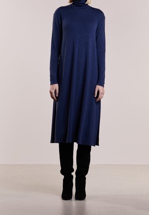 Robe longue bleu marine à manches longues avec un col roulé montant, une coupe ample, arrivant mi-mollet, avec des fentes latérales discrètes. À assortir avec des bottes noires montantes jusqu'aux genoux.