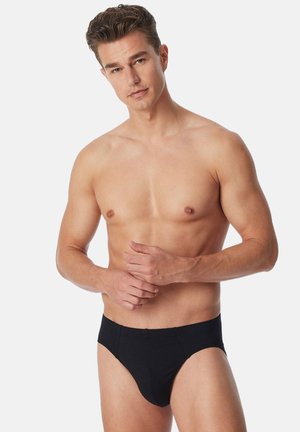 Schwarze Baumwollunterwäsche mit enganliegender Passform, die eine glatte Textur und ein minimalistisches Design aufweist, an einem Modell mit neutralem Ausdruck.