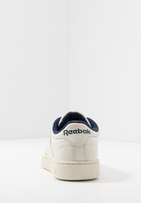 Zapatilla deportiva de cuero blanco con acentos en azul marino, punta redonda, suela texturizada, cuello acolchado y logo de Reebok en el talón.