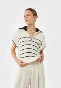 Sweter dziergany w kolorze kremowym z granatowymi poziomymi paskami, z krótkimi rękawami i kołnierzem na ćwierć zamka. Ribbowana faktura i luźny krój.