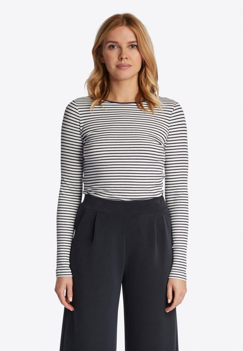 Zwart-wit gestreepte longsleeve top gecombineerd met hoge taille, donkere broeken. De top heeft een ronde halslijn en een geribbelde textuur.