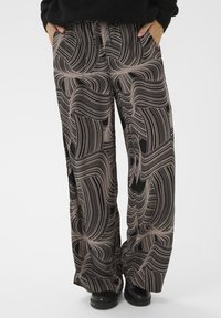 Pantalons larges en tissu léger, avec une base noire ornée de lignes ondulées abstraites en beige. Ceinture élastique et poches incluses.