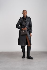 Sort læder trenchcoat med bælte i taljen, parret med sort støvler til knæene. En brun crossbody-taske har guldhardware.
