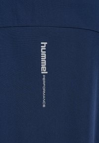 Marineblauw sportshirt met een gladde textuur, met een verticale zilveren "hummel" logo en de tekst "PERFORMANCE" op de voorkant.