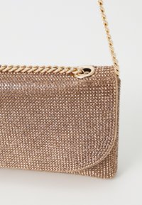 Rektangulær clutch-veske med et ytre dekket av rosegull og rhinestener. Har en gullkjede-rem og magnetisk klipslås.