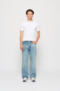 Hvit kortermet t-skjorte, avslappet passform lyseblå jeans og trening sneakers, står mot en enkel hvit bakgrunn.