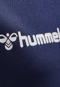 Mørkeblå tekstil med et fremtrædende hvidt "hummel" logo og en bi-grafik ovenfor, karakteriseret ved en glat, let tekstureret overflade.