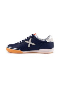 Zapatillas de lona marinas con cordones blancos, logo de acento gris, lado texturizado y una etiqueta naranja en la parte superior. Suela de goma en color marrón claro.