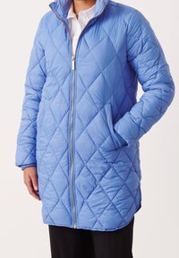 Cappotto imbottito trapuntato di colore azzurro chiaro, con una cerniera dorata, due tasche laterali e polsini a costine. Design lungo e oversize con colletto alto.