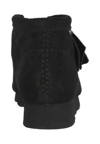 Svart mocka ankelskorn med en slät textur, sydda detaljer och en rosett-accent på sidan. Gummisulan ger bra grepp.