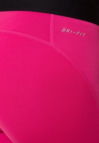 Gros plan de leggings de sport rose vif avec une ceinture noire et le texte « DRI-FIT » près de la couture supérieure.