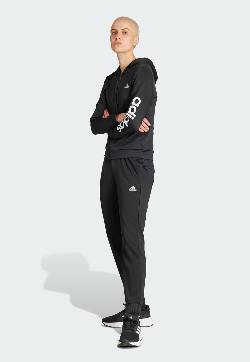 Czarny strój sportowy z zamkiem błyskawicznym, w tym bluza z kapturem z białym logo "adidas" na rękawie oraz dopasowane spodnie, zaprojektowany dla komfortu i swobody ruchów.