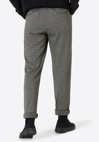 Graue Herringbone-Hosen mit aufgerollten Säumen, klassischer Schnitt und subtiler Textur. Kombiniert mit schwarzen Stiefeletten.