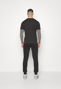 Černé sportovní tričko s šedými dlouhými rukávy, spárované s odpovídajícími černými joggingovými kalhotami. Má volný střih a kontrastní švy.