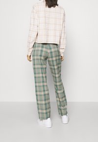 Zkrácená béžová kostkovaná košile s dlouhými rukávy spojená se zeleno-béžovými kostkovanými kalhotami s širokými nohavicemi, doplněná bílými teniskami.