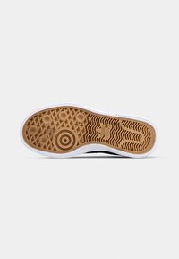 Shoe outsole featuring a gum rubber bottom with a textured grip pattern, white side edges, and a large circular logo detail.