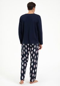 Granatowa koszulka z długim rękawem w zestawie z wzorzystymi spodniami od piżamy, na których znajduje się geometryczne wzory drzew w różowym i białym kolorze na ciemnym tle. Miękka tkanina, luźny krój.