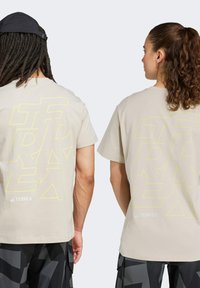 Camisetas beige con texto amarilla estilizado grande en la parte de atrás, combinadas con pantalones cortos oscuros y estampados. Mangas cortas y corte estándar.