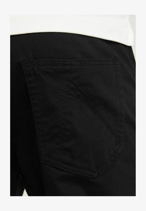 Mustad puuvillased püksid, millel on diagonaalne plaastritagumine tasku kontrastsete õmblustega. Sile tekstuur klassikalise lõikega ja minimalistliku disainiga.